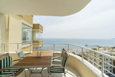 Alanya property balcony with wooden table, striped chairs, and stunning ocean views in a bright, airy atmosphere.
