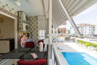 Μπαλκόνι σε ακίνητο στην Αλάνια με διακοσμητικούς τοίχους, σκούρο τραπέζι, κόκκινες καρέκλες και θέα στην πισίνα.
