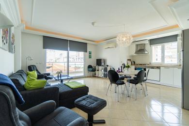 De heldere open woonkamer van dit Alanya-pand is voorzien van moderne meubels, een balkon met uitzicht en een strakke witte keuken.