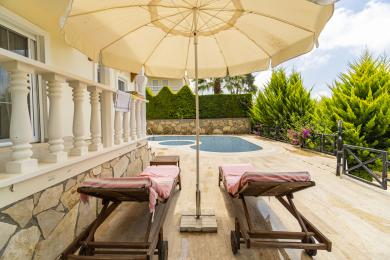 Alanya-Immobilien-Terrasse mit Sonnenliegen, Sonnenschirm und Pool, die einen entspannenden Außenbereich schafft.