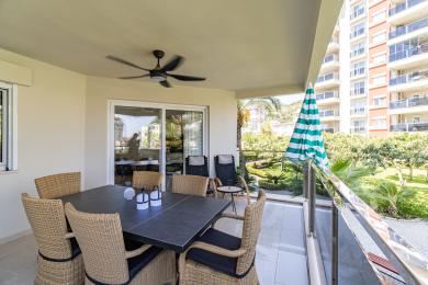 Balkon nemovitosti v Alanyi s proutěnou jídelní soupravou, stropním ventilátorem a světlou, vzdušnou atmosférou s výhledem na svěží zelené zahrady.