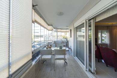 Der helle, geschlossene Alanya-Balkon verfügt über eine Essecke, einen Fliesenboden und raumhohe Fenster mit Plissees.