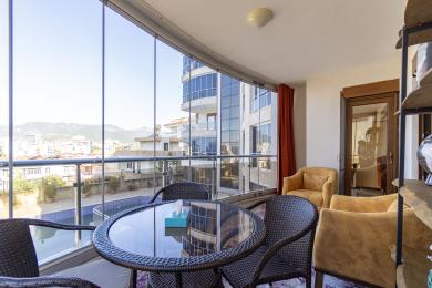 Proprietate în Alanya: Balcon închis cu pereți de sticlă, mobilier din răchită și atmosferă luminoasă și aerisită, cu vedere la oraș.
