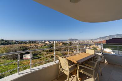 Alanya woning balkon met buitenset en panoramisch uitzicht op de stad en de zee, badend in zonlicht.