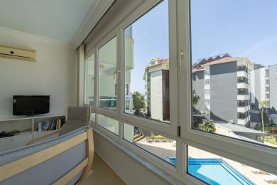 Lys Alanya hagestue med stort vindu med utsikt over bassenget, komfortable sitteplasser og moderne, minimalistisk innredning.