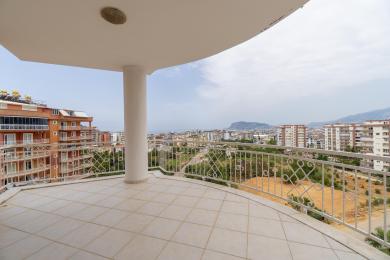 Alanya ingatlan erkély csempézett padlóval, fehér korlátokkal és panorámás városi kilátással természetes fényben.