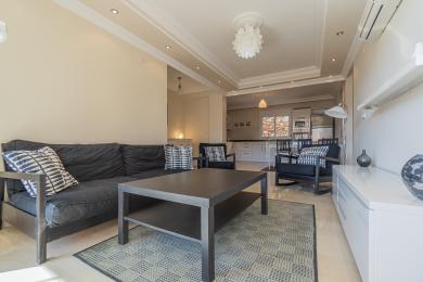 El salón de esta propiedad en Alanya cuenta con muebles modernos, tonos neutros y una cocina de planta abierta, creando un ambiente luminoso y aireado.