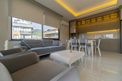 Salon w Alanyi z nowoczesną szarą sofą, częścią jadalną i elegancką kuchnią z ciepłym oświetleniem.