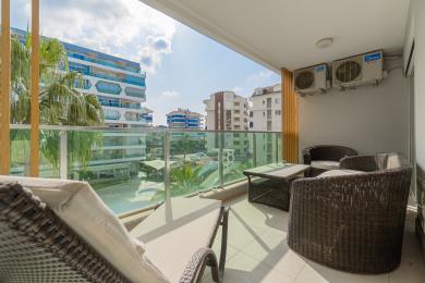 Alanya woning balkon met wicker meubilair, glazen balustrades en helder, zonnig uitzicht op nabijgelegen gebouwen.