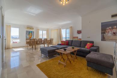 Un living luminos în Alanya, cu podele de marmură, o canapea gri, o zonă de luat masa și vederi expansive asupra mării vizibile prin ferestre mari.