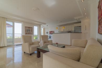Bright Alanya living room featuring marble floors, neutral furniture, and an open-plan kitchen illuminated by recessed lighting, creating a relaxed atmosphere.