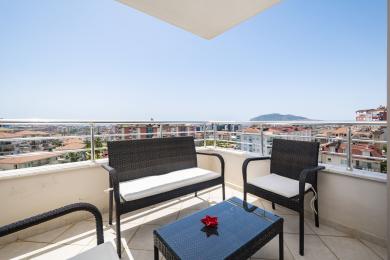 Balkon nekretnine u Alanji s namještajem od pruća, bijelim jastucima i panoramskim pogledom na grad pod jarkim suncem.