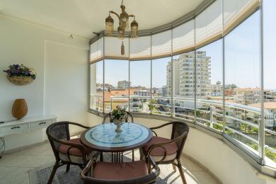 A varanda luminosa de Alanya apresenta um recinto de vidro, móveis de vime, piso de cerâmica e vistas da cidade.