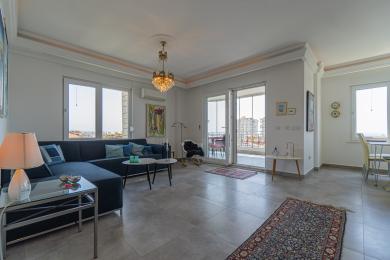 明るいアパートのリビングルームは、バルコニーにアクセスでき、街の景色とエレガントなシャンデリア照明が特徴です。