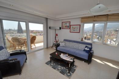 Sala de estar luminosa do apartamento em Alanya com acesso à varanda, pisos de cerâmica e vistas da cidade a partir de grandes janelas.