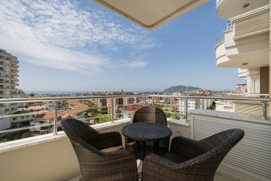 Alanya'da hasır mobilyalarla döşenmiş, parlak bir gökyüzü altında muhteşem şehir ve deniz manzaralı balkon.
