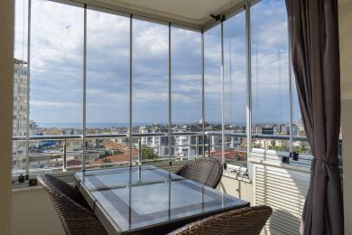 Lukket altan i Alanya med glasvægge, kurvemøbler og havudsigt.