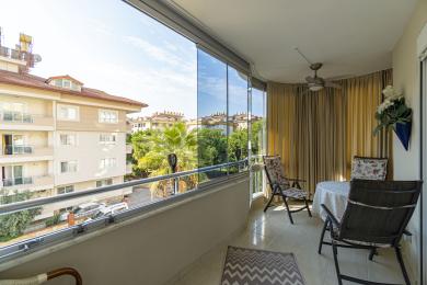 Alanya eiendom balkong med glassvegger, flislagt gulv, sitteplasser og lys, luftig atmosfære med utsikt over byen.