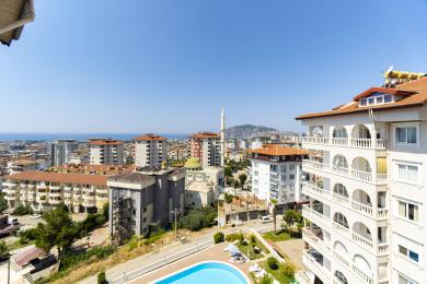 Alanya woning balkon uitzicht met uitzicht op de stad, de zee en het zwembad onder een heldere, zonnige hemel.