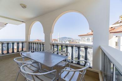 Balcone di proprietà ad Alanya con aperture ad arco, vista sulla città e tavolo e sedie in metallo in piena luce diurna.