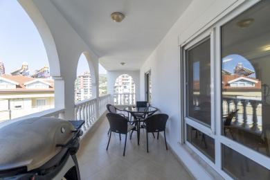 Balkon w Alanyi z białymi łukami, kafelkową podłogą, miejscami do siedzenia na zewnątrz oraz jasną, przestronną atmosferą.