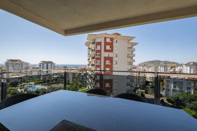Balkon nekretnine u Alanji s namještajem od pruća nudi zadivljujući pogled na grad pod jarkim, prirodnim svjetlom.