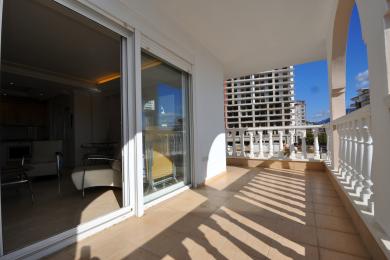 Balcone di proprietà ad Alanya con pavimenti in piastrelle, balaustra bianca e luce solare intensa, che offre viste sulla città.