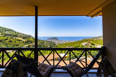 Balcón de la propiedad de Alanya con barandilla de madera que ofrece impresionantes vistas al mar y a la montaña, creando un ambiente relajante.