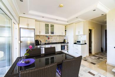 Cozinha de propriedade em Alanya com armários brancos, eletrodomésticos de aço inoxidável e uma moderna área de jantar banhada em luz natural.
