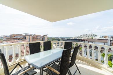 Balkon nekretnine u Alanji sa pogledom na grad, sa staklenim stolom, stolicama od pruća i svetlom, prozračnom atmosferom.