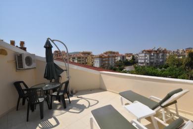 Proprietate în Alanya cu balcon cu podea de gresie, șezlonguri, set de luat masa și vedere la oraș sub un cer luminos.
