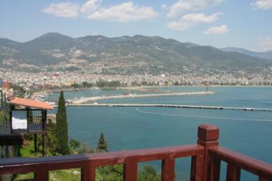 Alanya ejendom balkon med trærækværk med udsigt over det turkisblå hav og byens skyline, badet i skarpt sollys.