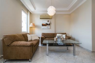 A sala de estar da propriedade em Alanya apresenta sofás castanhos, mesa de vidro, piso de cerâmica e iluminação suave e neutra, criando uma atmosfera acolhedora.