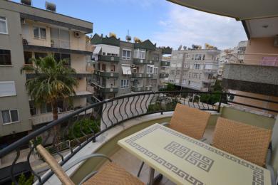 Alanya property balcony with wicker chairs, table, and wrought iron railing offering city views.