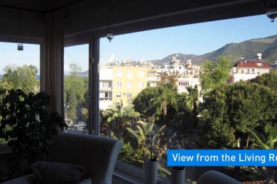Alanya property living room view showcases lush greenery and distant mountains through bright, expansive windows.