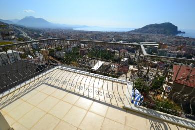 Balkon nemovitosti v Alanyi s dlaždicovou podlahou, zdobným železným zábradlím a panoramatickým výhledem na město a pobřeží.