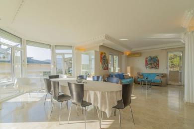 A luminosa sala de estar em Alanya apresenta pisos de mármore, grandes janelas, área de jantar e assentos confortáveis com obras de arte coloridas.